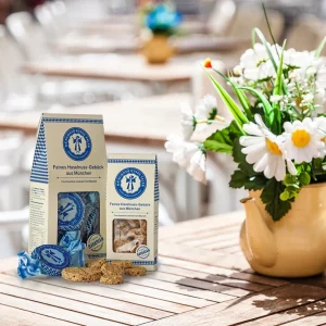 Verpackungen des Münchner Kindl-Talers auf einem Holztisch im Café mit Blumenvase